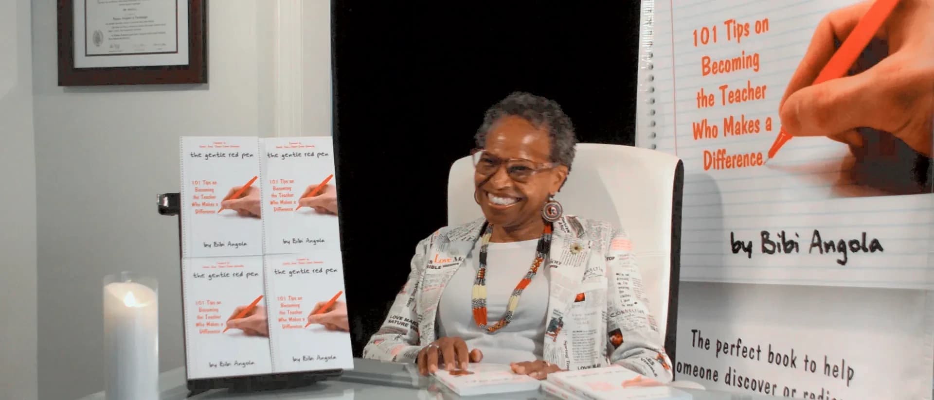 Bibi Angola smiling at her desk, her framed diploma on the wall behind her